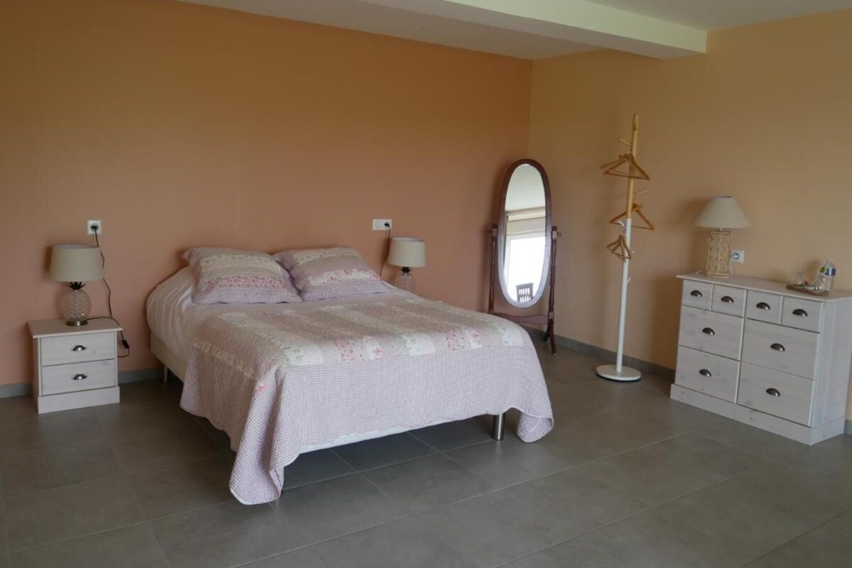 Un dormitorio con cama, mesitas de noche, cómoda, espejo y lámpara de pie.