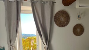 Un dormitorio con cama, cortinas, vistas al verdor exterior y un techo con vigas a la vista.