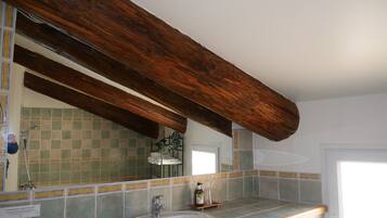 A bathroom with a large mirror, wooden beams, a sink, and tiled walls.