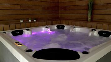 Un jacuzzi con varias zonas de descanso, rodeado de paredes de madera y pequeñas macetas.