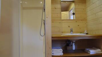 A wooden cabin bathroom with a shower, sink, mirror, and towel storage.