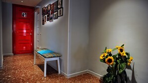 Un pasillo con una puerta roja, un banco con un cojín estampado y una pared con cuadros enmarcados.