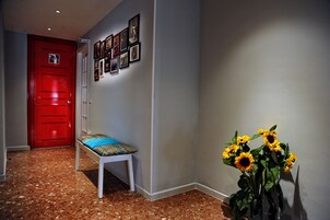 A hallway with a red door, a bench with a patterned cushion, and a wall with framed pictures.