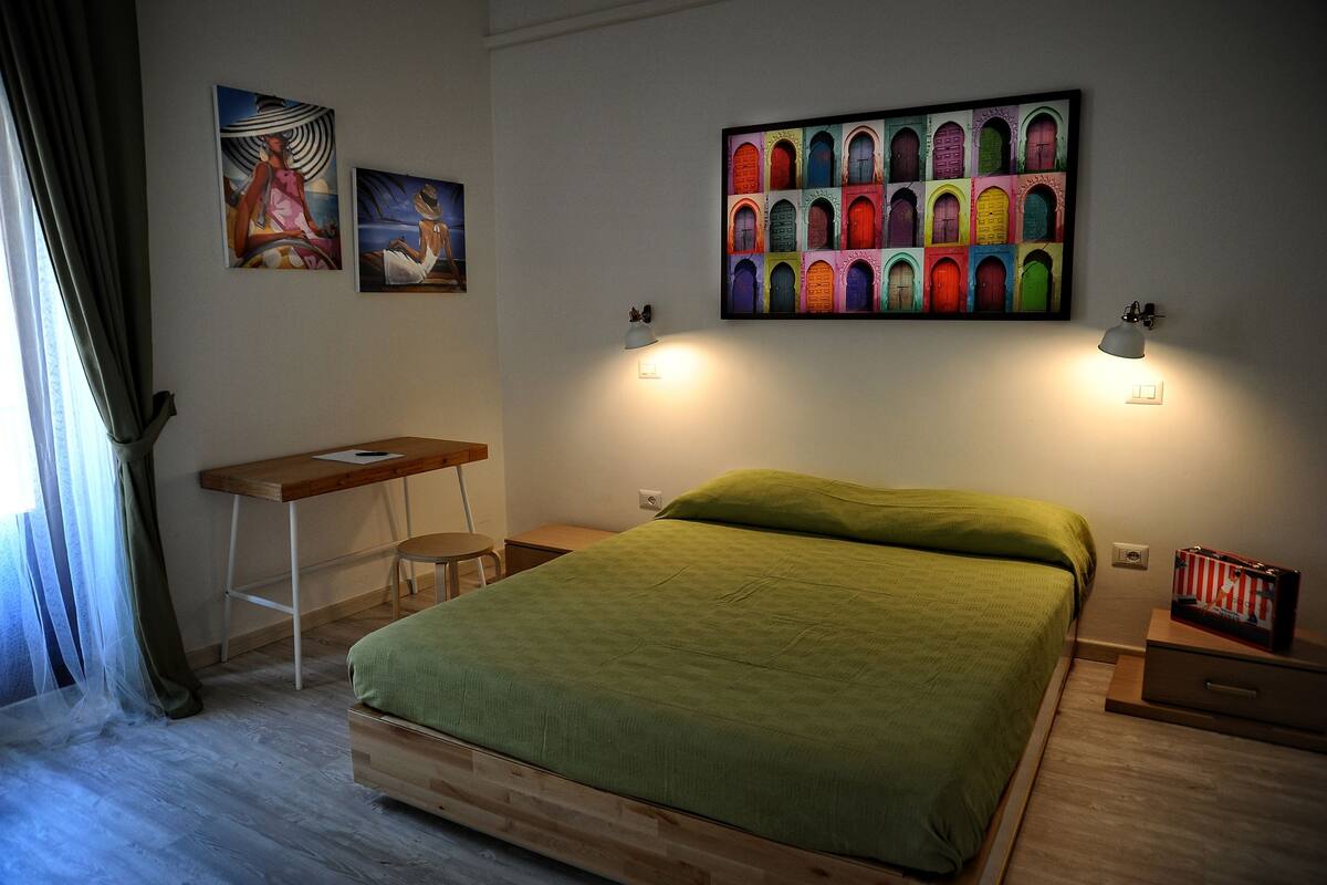A bedroom with a bed, a desk, and two wall-mounted lamps.
