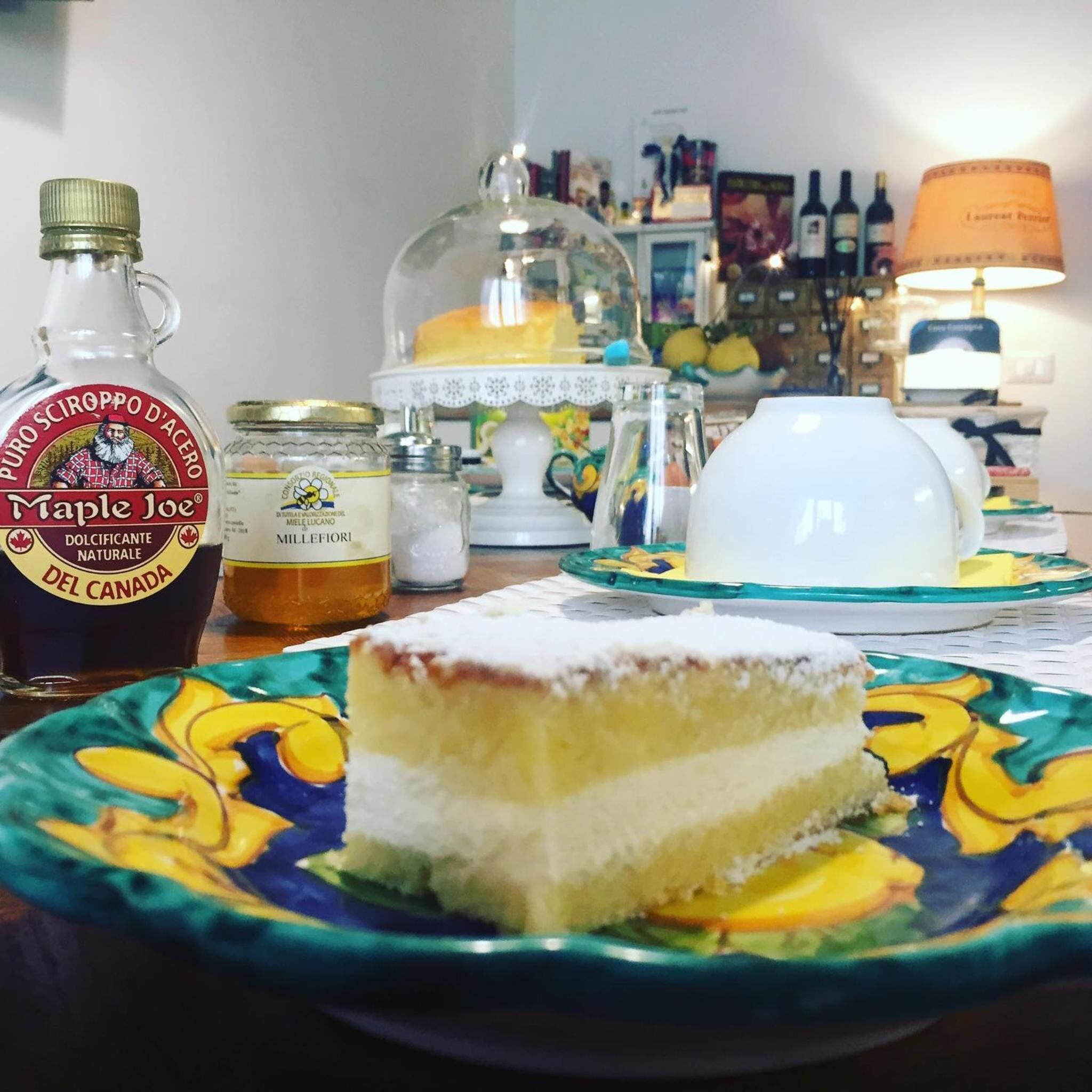 Una mesa con una porción de pastel, una botella de sirope de arce y una tetera.