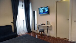 Habitación de hotel con cama, escritorio con silla, televisor montado en la pared y una puerta.
