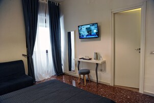 A hotel room with a bed, a desk with a chair, a television mounted on the wall, and a door.