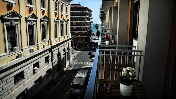 Vista desde un balcón que muestra un edificio de varios pisos, cielo despejado y un autobús estacionado.