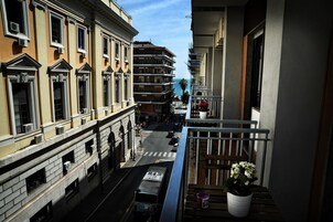 A street view from a balcony with a view of a multi-story building, a clear sky, and a parked bus.