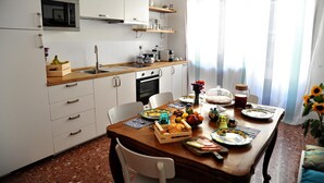 Cocina compacta con armarios blancos, encimera de madera y una mesa de comedor dispuesta con frutas y una máquina de café.