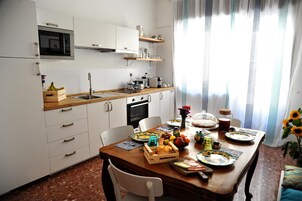 Cocina compacta con armarios blancos, encimera de madera y una mesa de comedor dispuesta con frutas y una máquina de café.