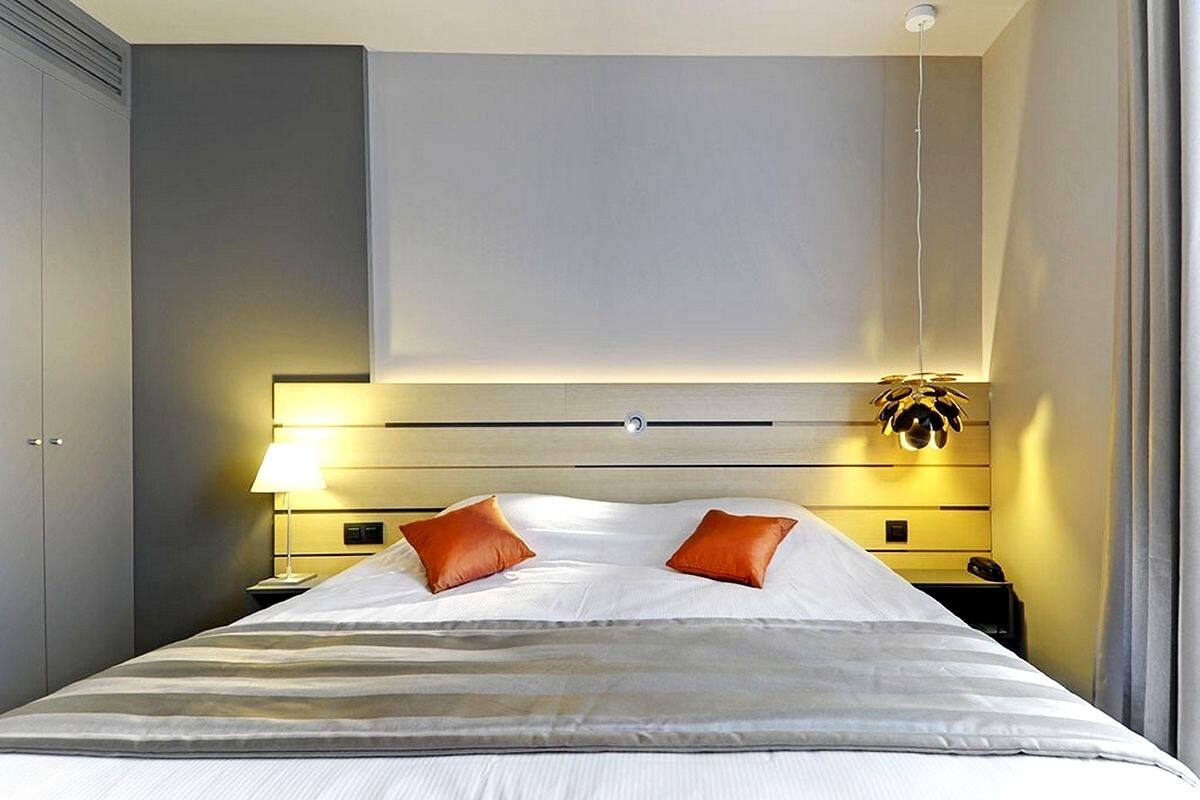 A modern hotel room with a large bed, two pillows, a bedside table with a lamp, and a nightstand with a phone.