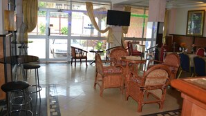 A restaurant with wicker furniture, a TV mounted on the wall, and a view of the street outside. - Hotel Le Diplomate (Yaoundé)