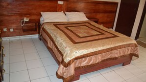 A wooden bed with a quilt, a bedside table, and a telephone. - Hotel Le Diplomate (Yaoundé)