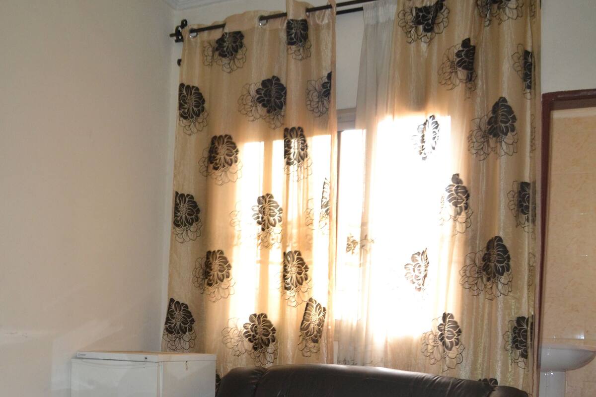 A living room with a leather sofa, a glass coffee table with a floral vase, a white radiator, and a bathroom with a sink and toilet.