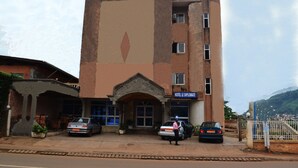 A hotel with a prominent entrance, a sign reading "HOTEL LE DIPLOMAT," and two cars parked in front. - Hotel Le Diplomate (Yaoundé)