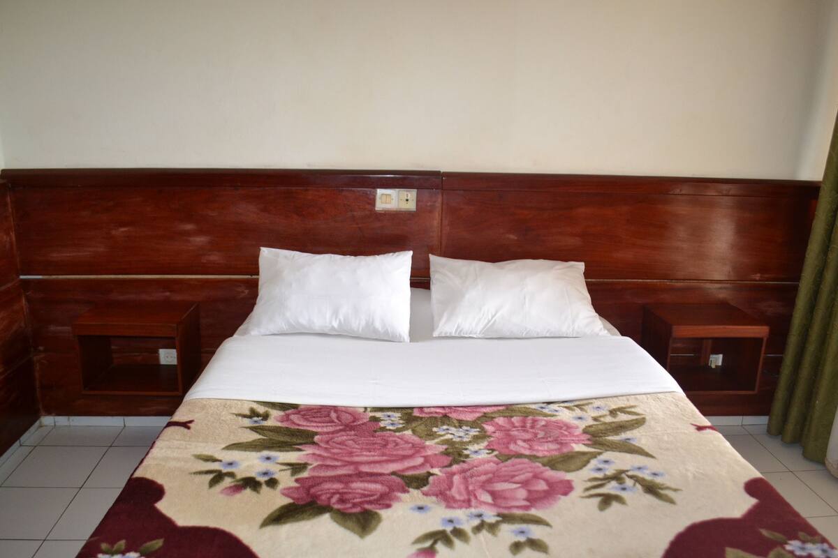 A bed with a floral bedspread, two white pillows, wooden headboard, and nightstands with lamps.
