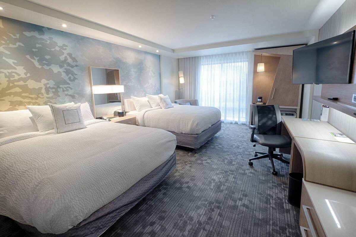 Une chambre d’hôtel avec deux lits, un bureau, une télévision et une grande fenêtre avec des rideaux.
