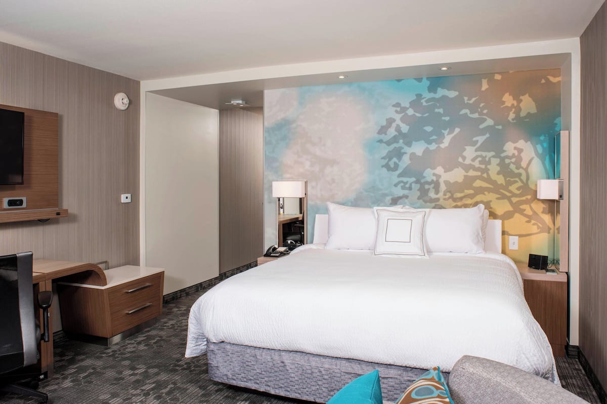 Une chambre d’hôtel avec un grand lit, un bureau, une chaise, une télévision et un mur orné d’un motif de camouflage.