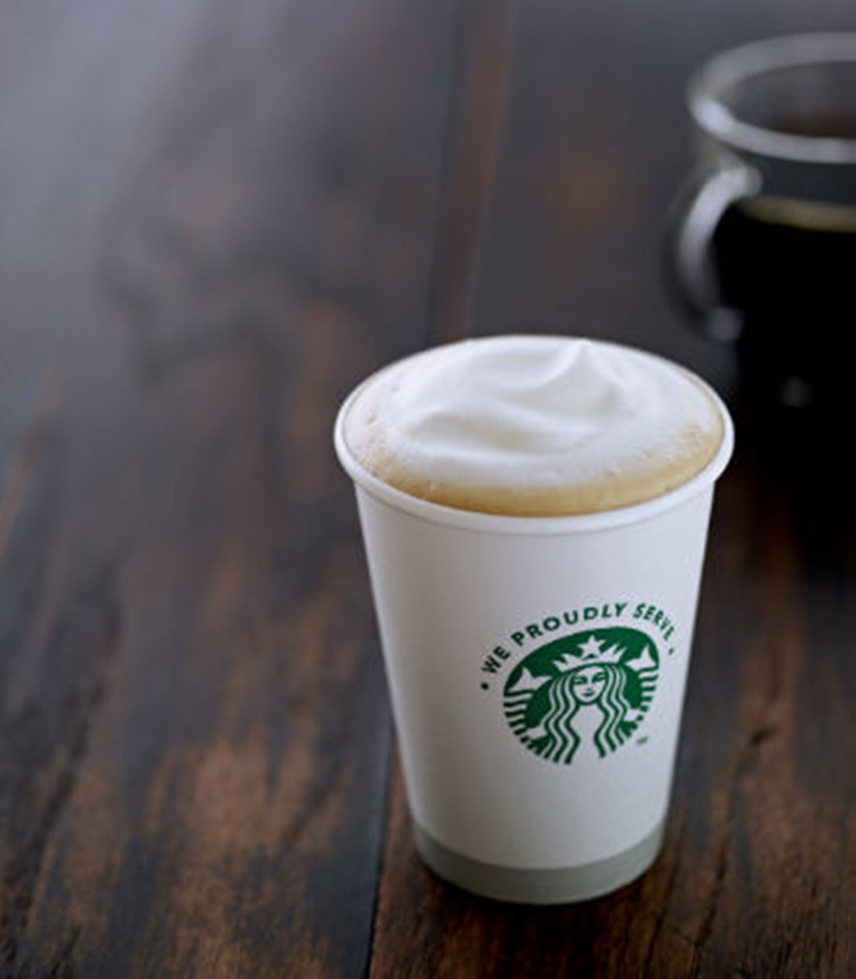A Starbucks cup with a frothy top on a wooden table.
