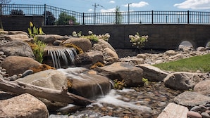 A stone bridge with a metal railing, a small waterfall, and a rocky stream. - Courtyard by Marriott Albany Clifton Park (Clifton Park)