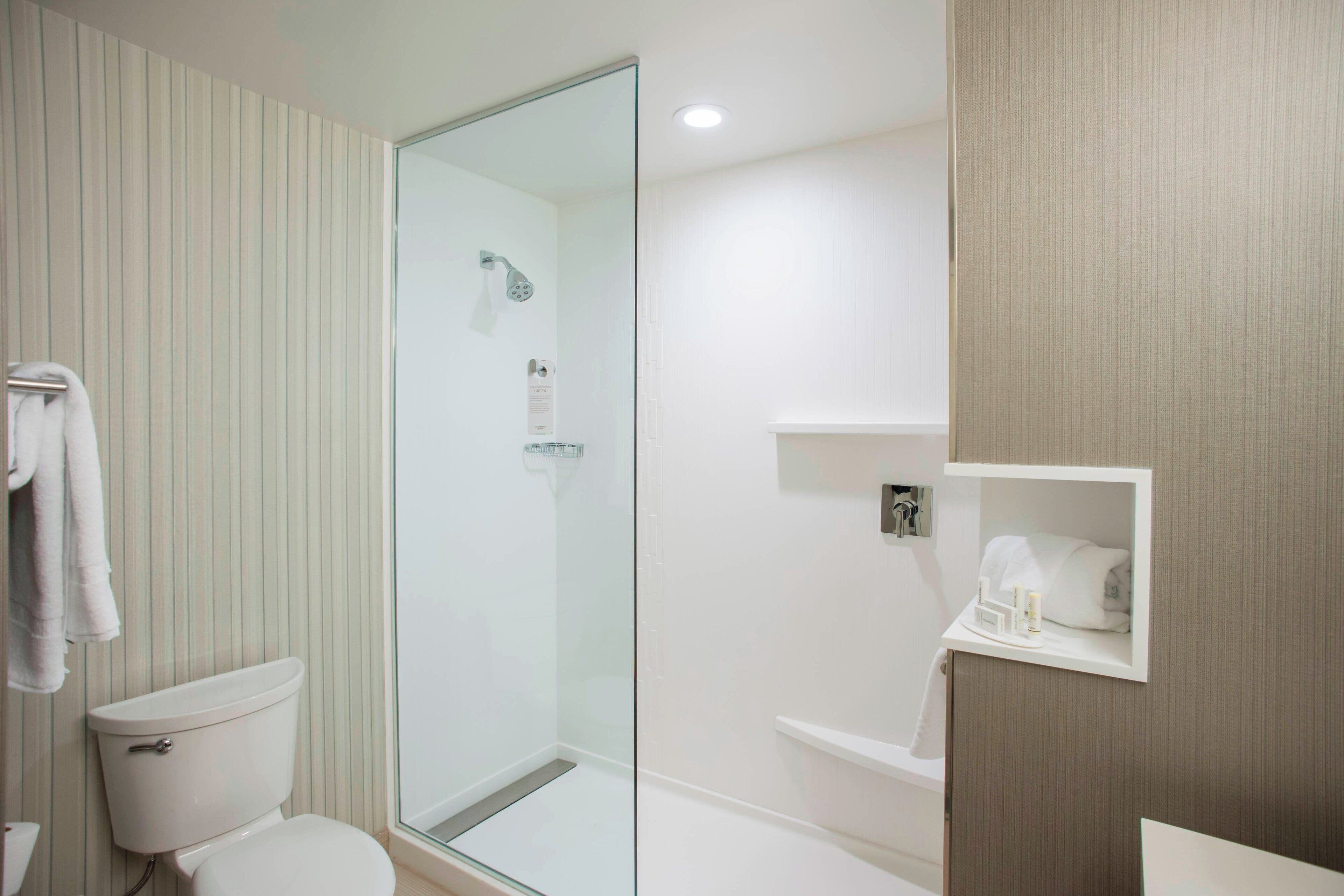 Un baño moderno con ducha de vidrio, inodoro y tocador con barra para toallas.