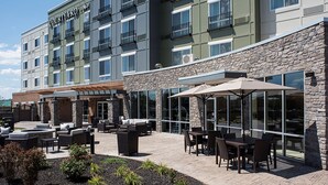 A Courtyard Mar hotel with outdoor seating, stone walls, and large windows. - Courtyard by Marriott Albany Clifton Park (Clifton Park)