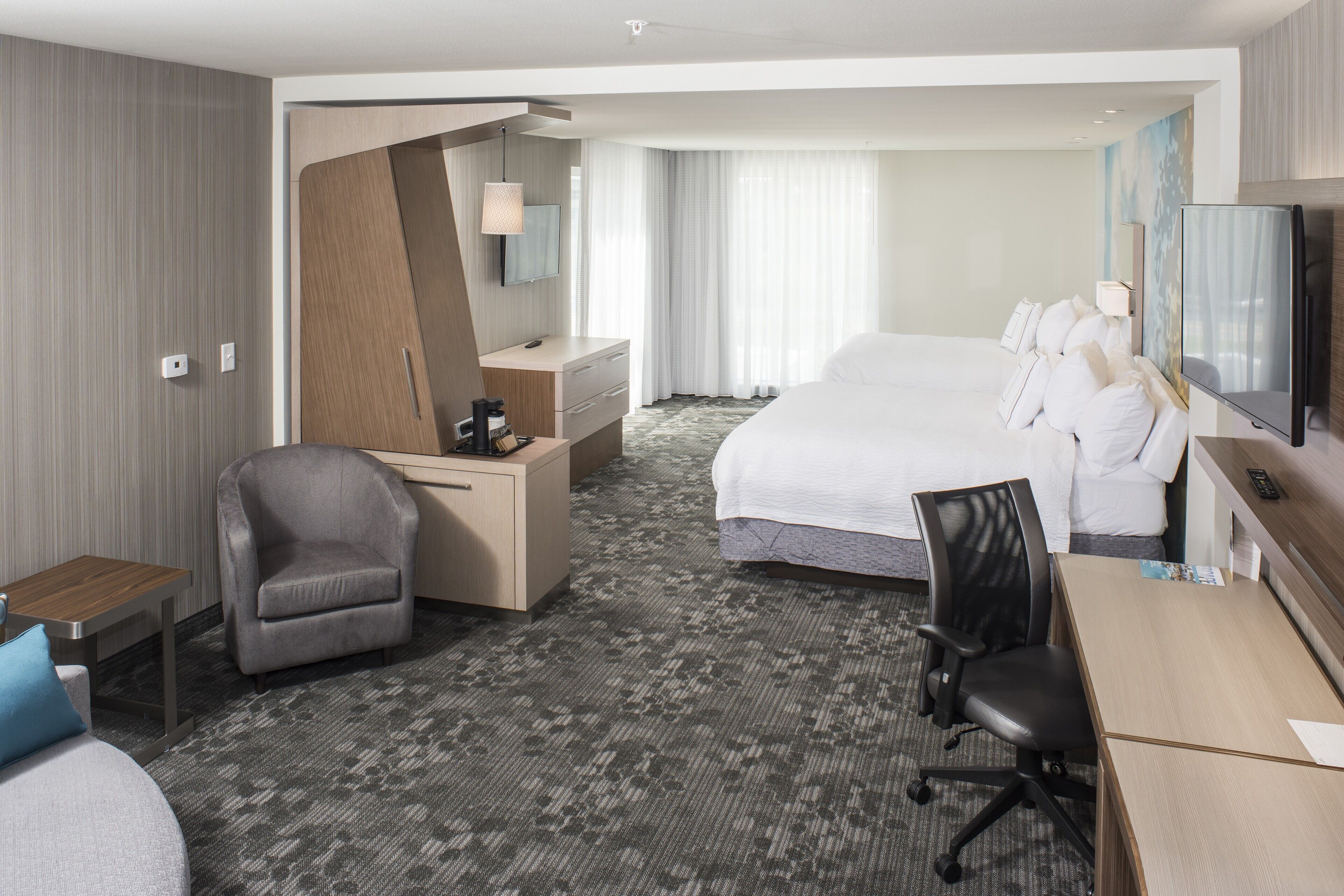 Habitación de hotel con una cama grande, un escritorio, una silla, un televisor y un espejo.