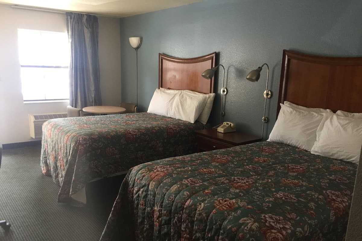Una habitación de hotel con dos camas, una mesita, una silla, una lámpara y un teléfono.