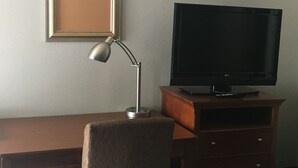 A hotel room with a flat-screen TV on a wooden stand, a framed picture on the wall, and a desk with a lamp. - Sunset Inn (West Memphis)
