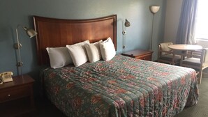 A hotel room with a large bed, two bedside tables, a desk with a chair, and a small round table with a chair. - Sunset Inn (West Memphis)