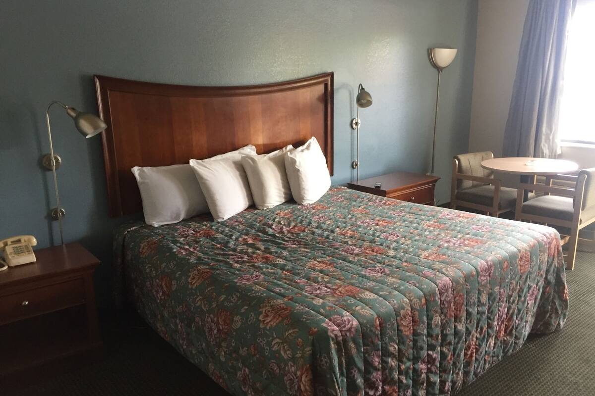 Habitación de hotel con una cama grande, dos mesitas de noche, un escritorio con una silla y una pequeña mesa redonda con una silla.