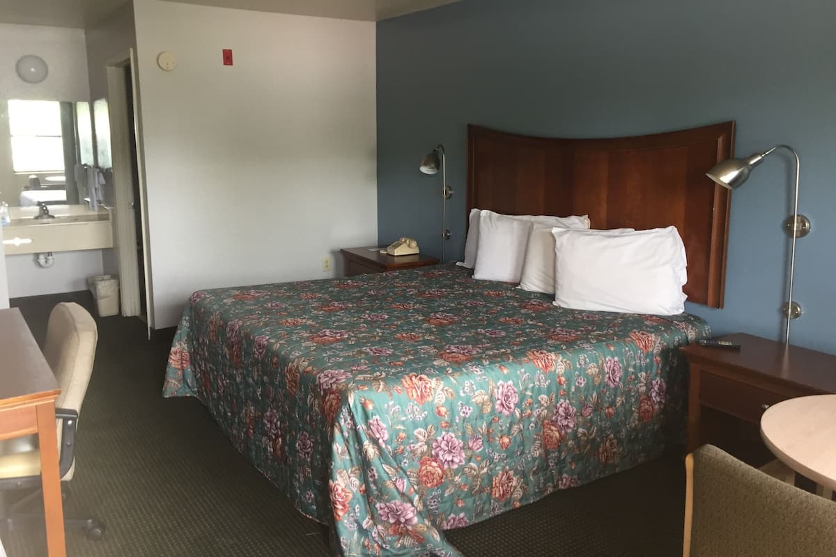 Una habitación de hotel con una cama, un escritorio, una silla, una mesita de noche y una lámpara.