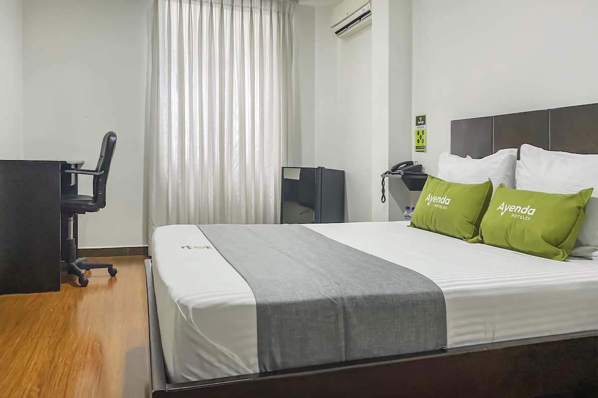 A hotel room with a bed, a desk, a chair, and a window with curtains.