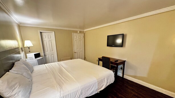 Quarto de hotel com uma cama grande, uma escrivaninha com cadeira, uma televisão na parede e duas portas.