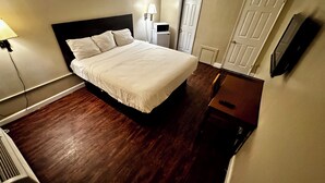 Quarto de hotel com uma cama grande, mesa de cabeceira, escrivaninha, luminária e televisão na parede.