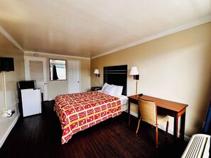 A hotel room with a bed, a desk, a chair, a small refrigerator, and a window with blinds. - Downbeach Inn (Atlantic City)
