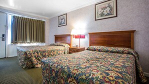 Quarto de hotel com duas camas, cabeceira de madeira, mesa de cabeceira, abajur e arte floral na parede.