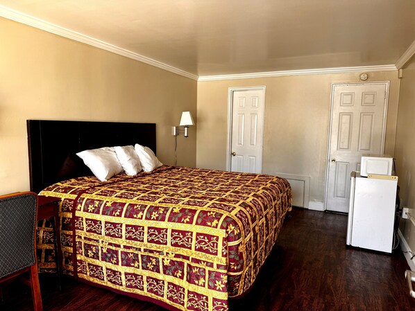 A hotel room with a large bed, a desk, a chair, and a refrigerator. - Downbeach Inn (Atlantic City)