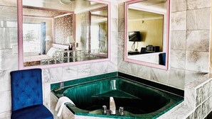 Uma casa de banho com um espelho grande, uma banheira de hidromassagem verde e uma cadeira azul.