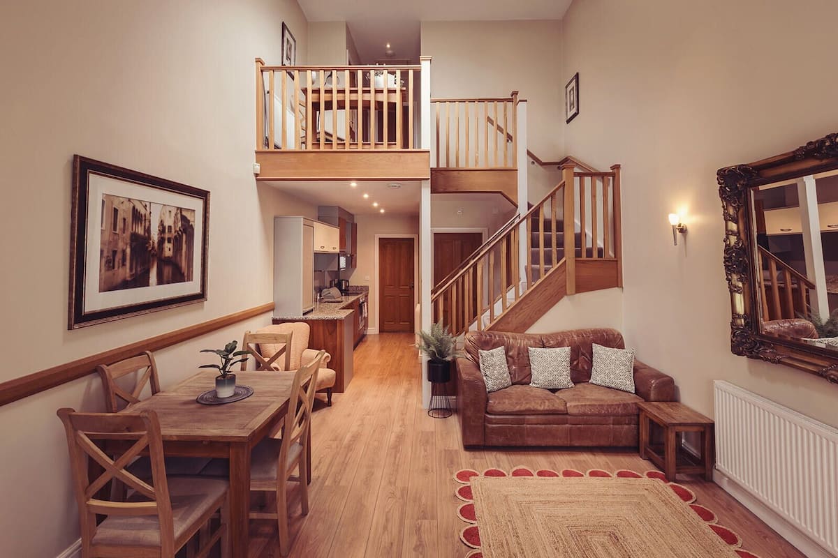 Un vaste espace de vie comprenant un escalier en bois, une table à manger avec des chaises, un canapé et un grand miroir.