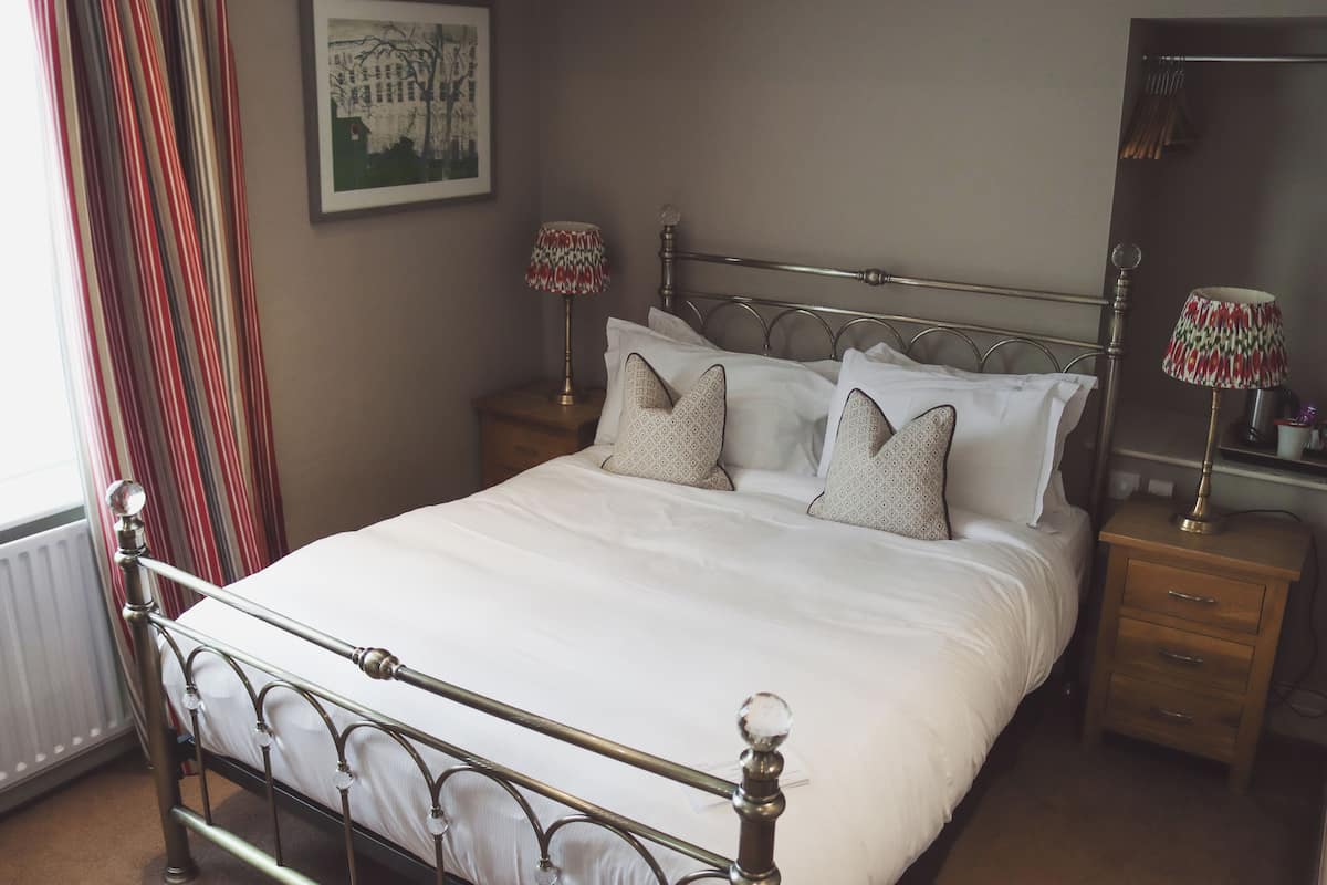 Un lit bien fait, avec du linge de lit blanc et des coussins décoratifs, un lit en métal avec une tête de lit en bois, deux tables de chevet avec des lampes et un tableau encadré au mur.