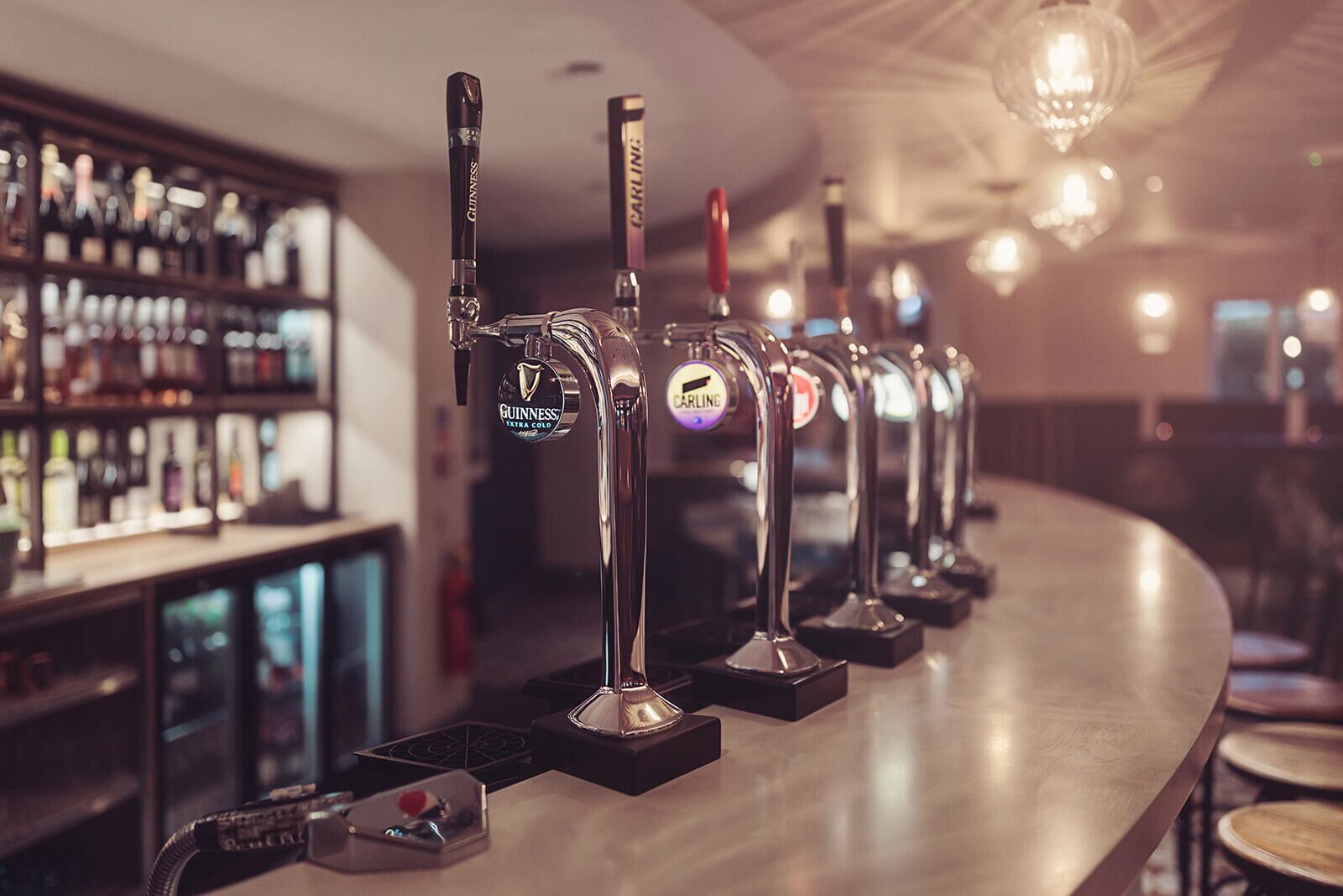 A bar with multiple taps, including Guinness and Carling, and a well-stocked shelf of bottles.