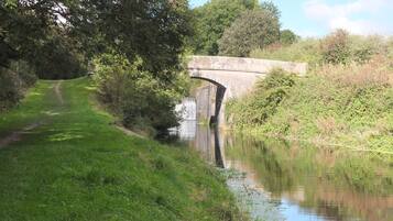 A stone bridge over a calm river, surrounded by lush greenery and a grassy path.