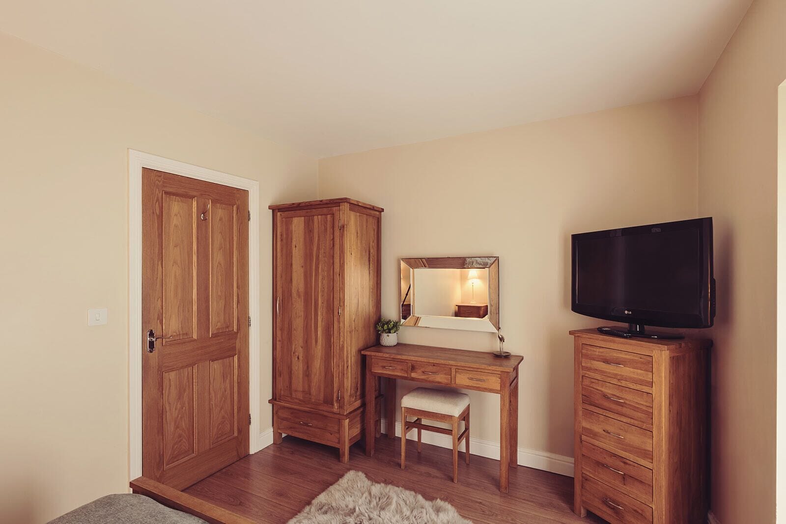 Ein Schlafzimmer mit einem Holzschrank, einem Schreibtisch mit Spiegel, einem Fernseher und einem kleinen Stuhl.