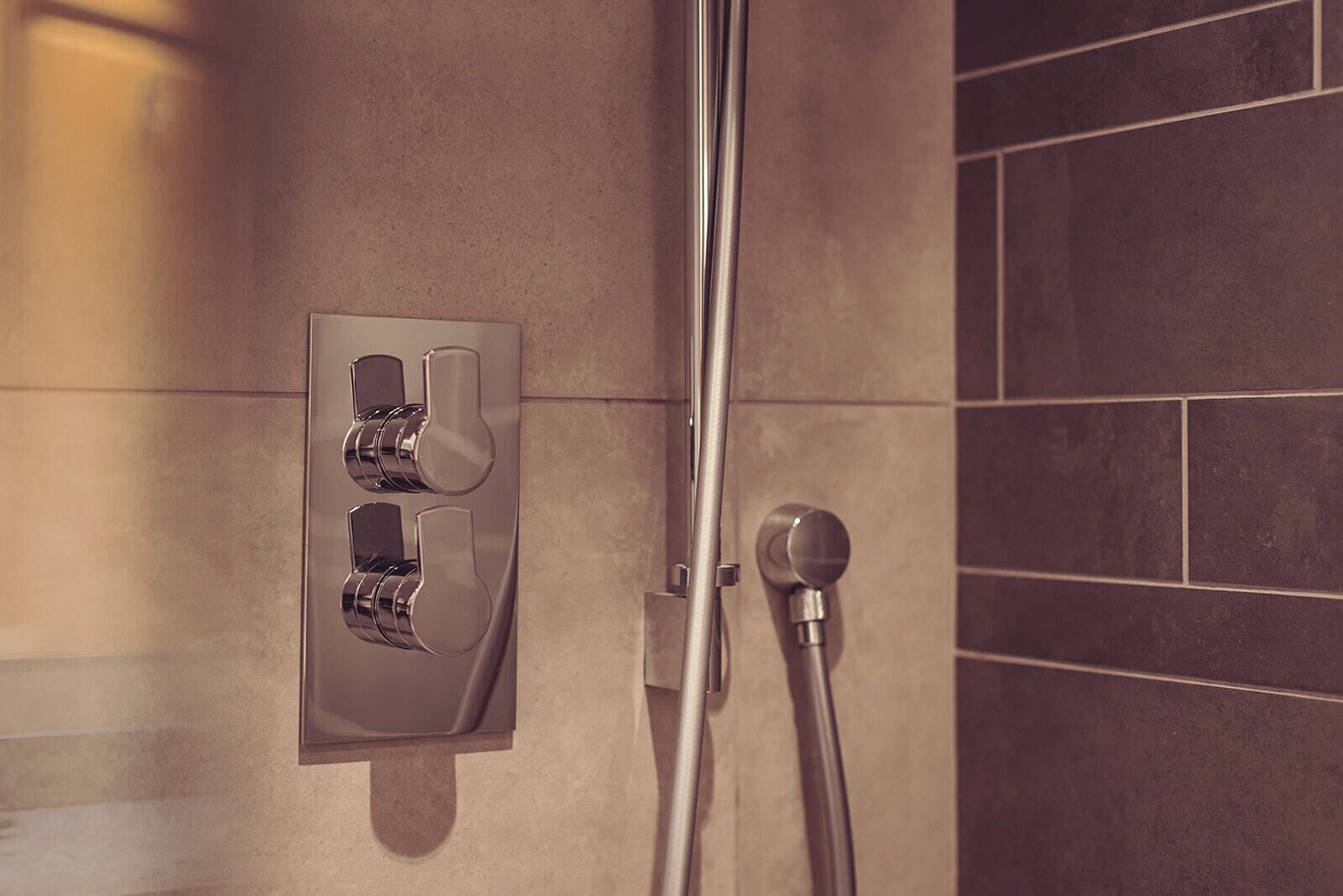 A shower with a wall-mounted control panel and a handheld showerhead.