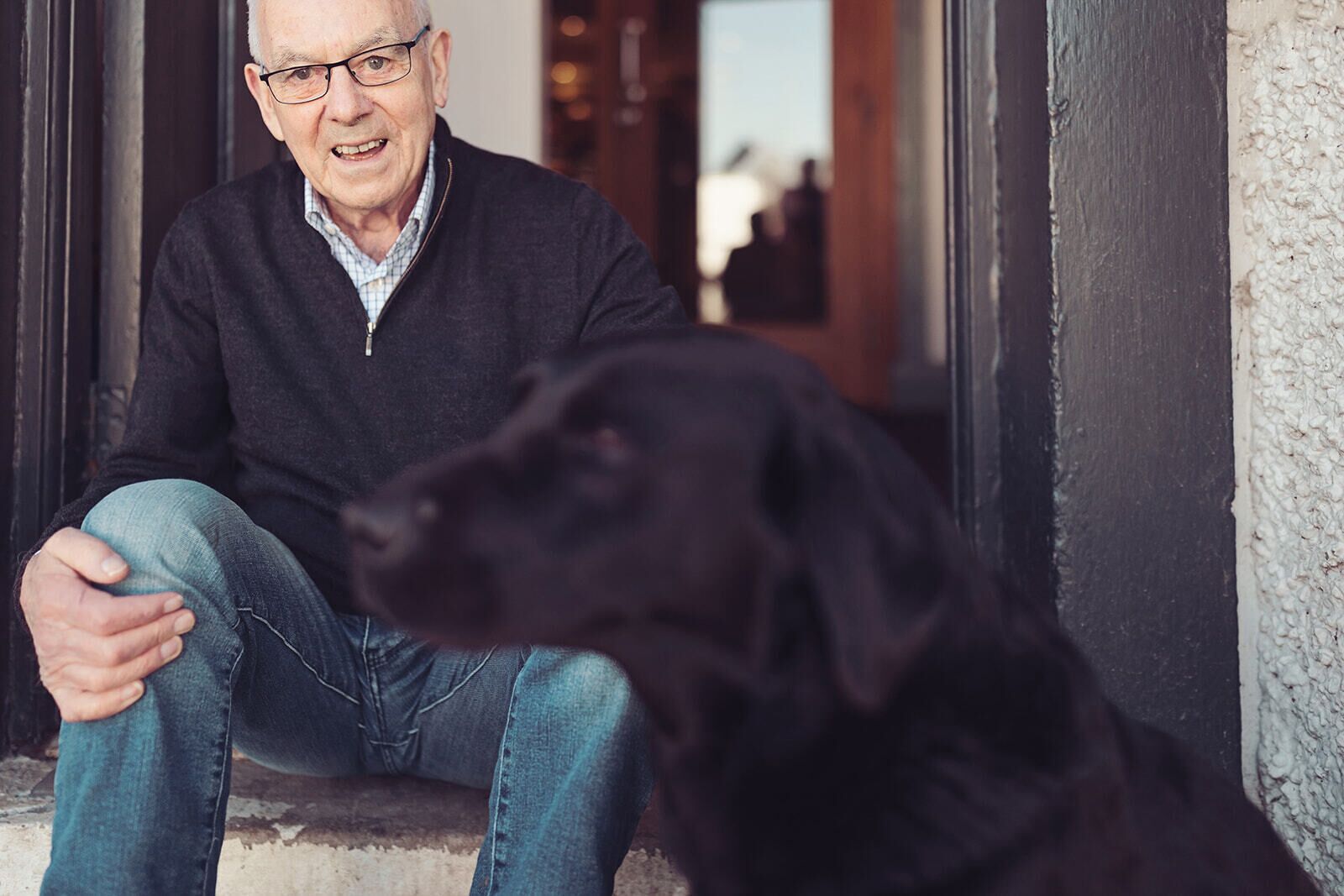 A person sitting on steps with a black dog.