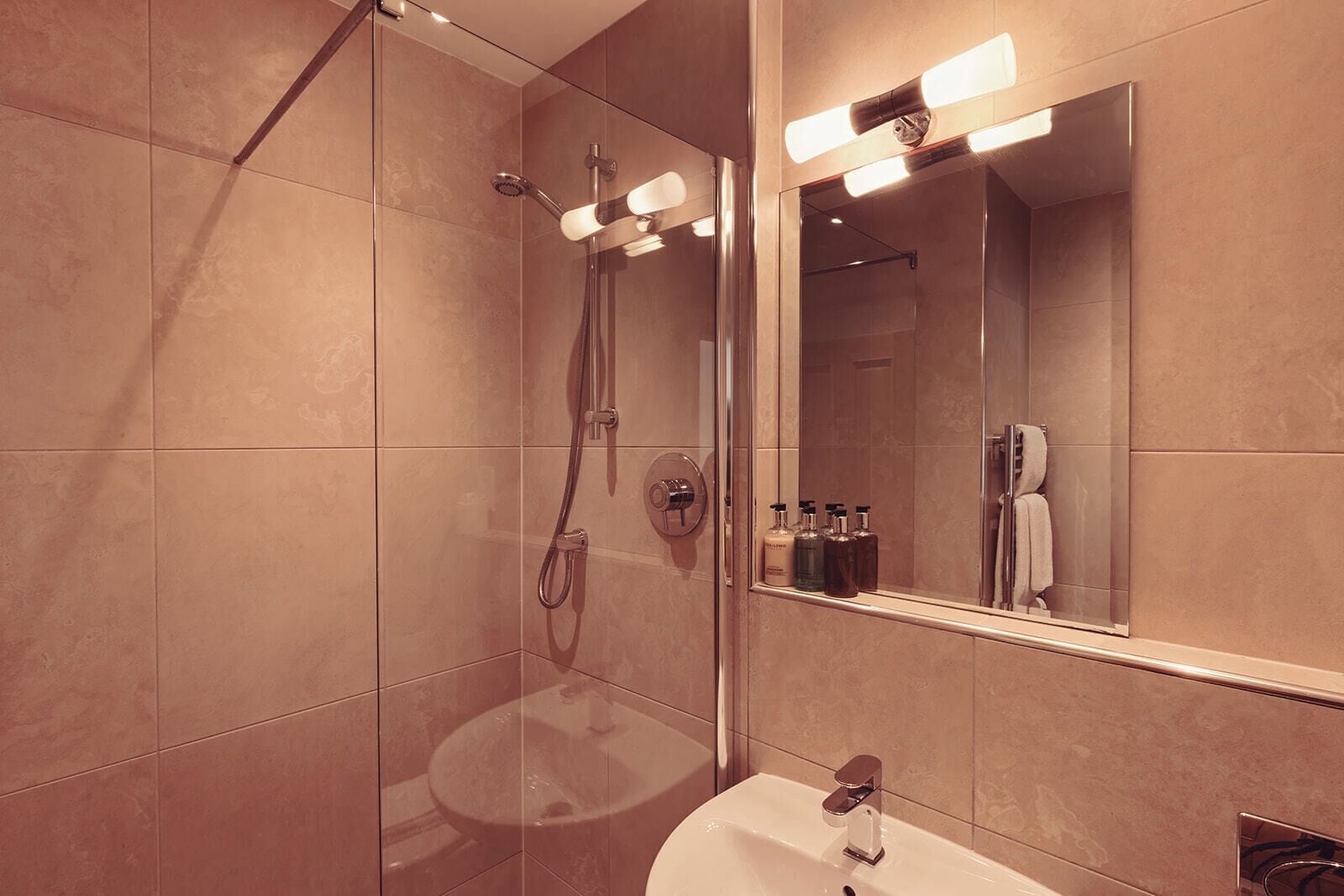 Un baño moderno con ducha de vidrio, tocador con lavabo y espejo con iluminación integrada.