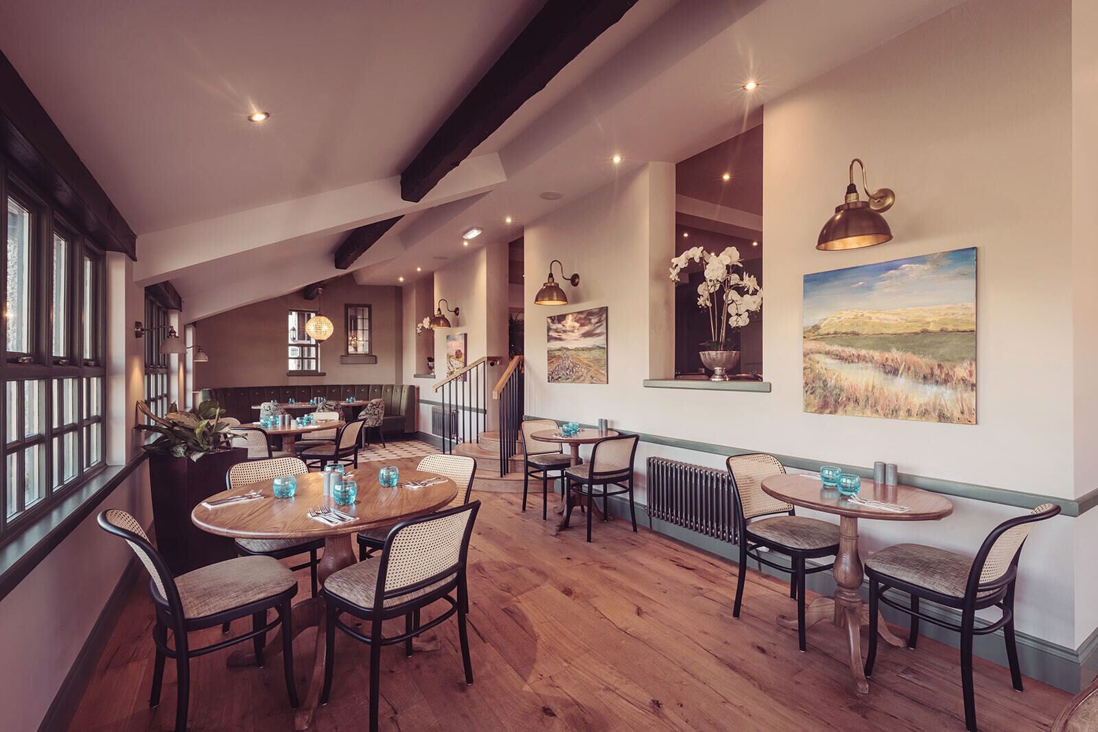 A restaurant with round tables, wooden floors, and pendant lighting.