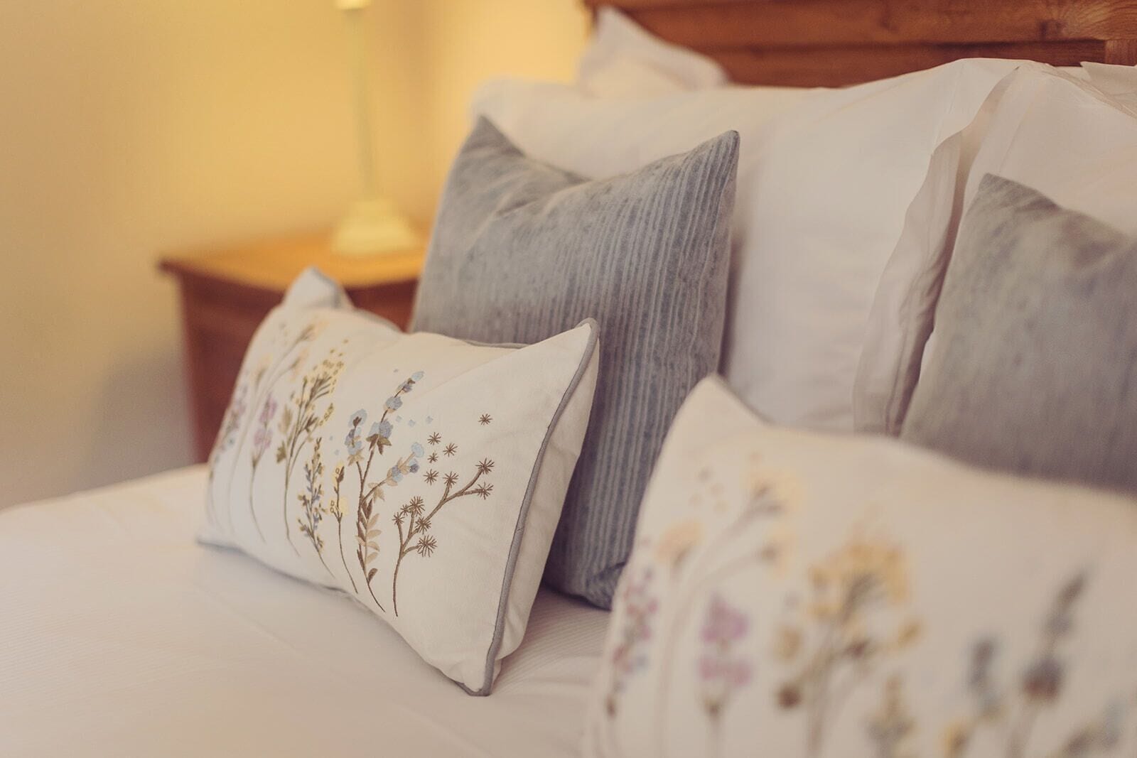 Una cama con varias almohadas, un cabecero de madera y una mesita de noche con una lámpara.